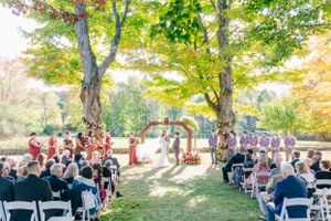 Beautiful outdoor wedding ceremony with guests seated on white chairs under autumn trees.