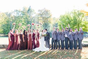Wedding party in burgundy dresses and gray suits celebrates under autumn trees.