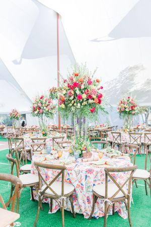 Garden wedding reception with white tent, floral centerpieces and cross-back chairs.