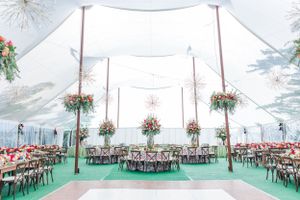 An elegant white tent reception setup with floral arrangements and chandelier lighting.