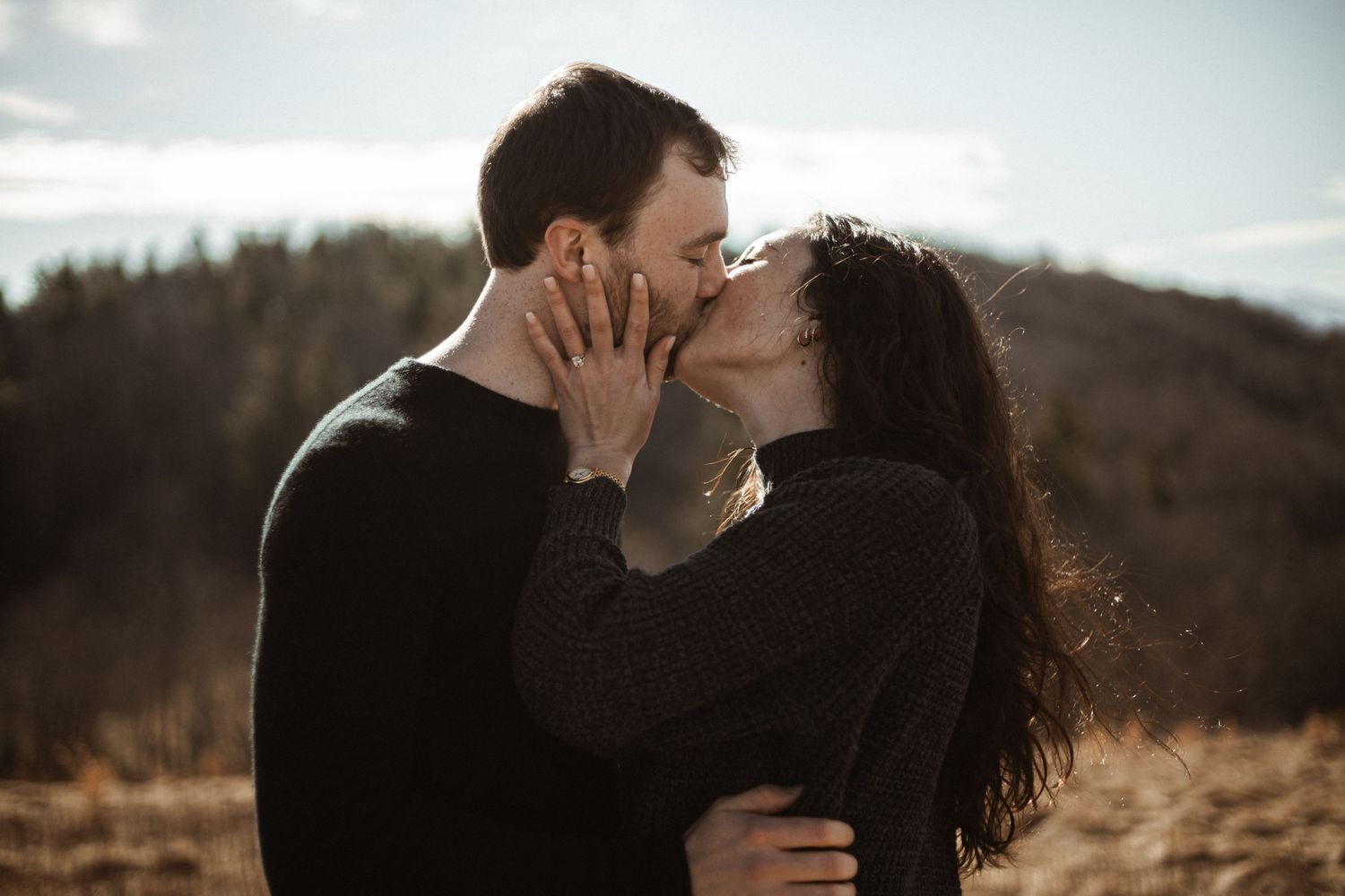 A tender intimate moment between a couple kissing outdoors against a mountainous backdrop.