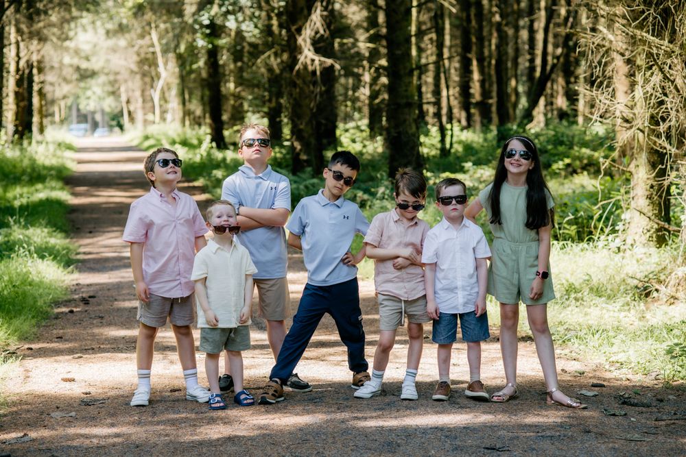 Group of children wearing sunglasses posing together on a forest path in a sunny outdoor setting. Center Parcs Longford Forest