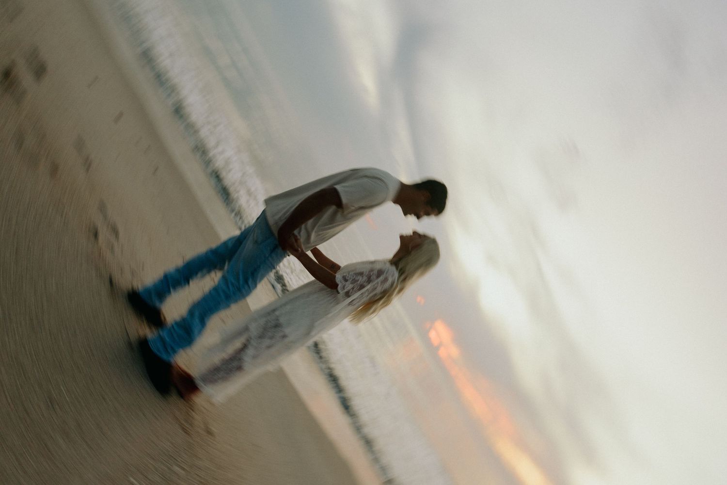 Couple sharing a romantic kiss on a sandy beach at sunset with ocean waves in the background.