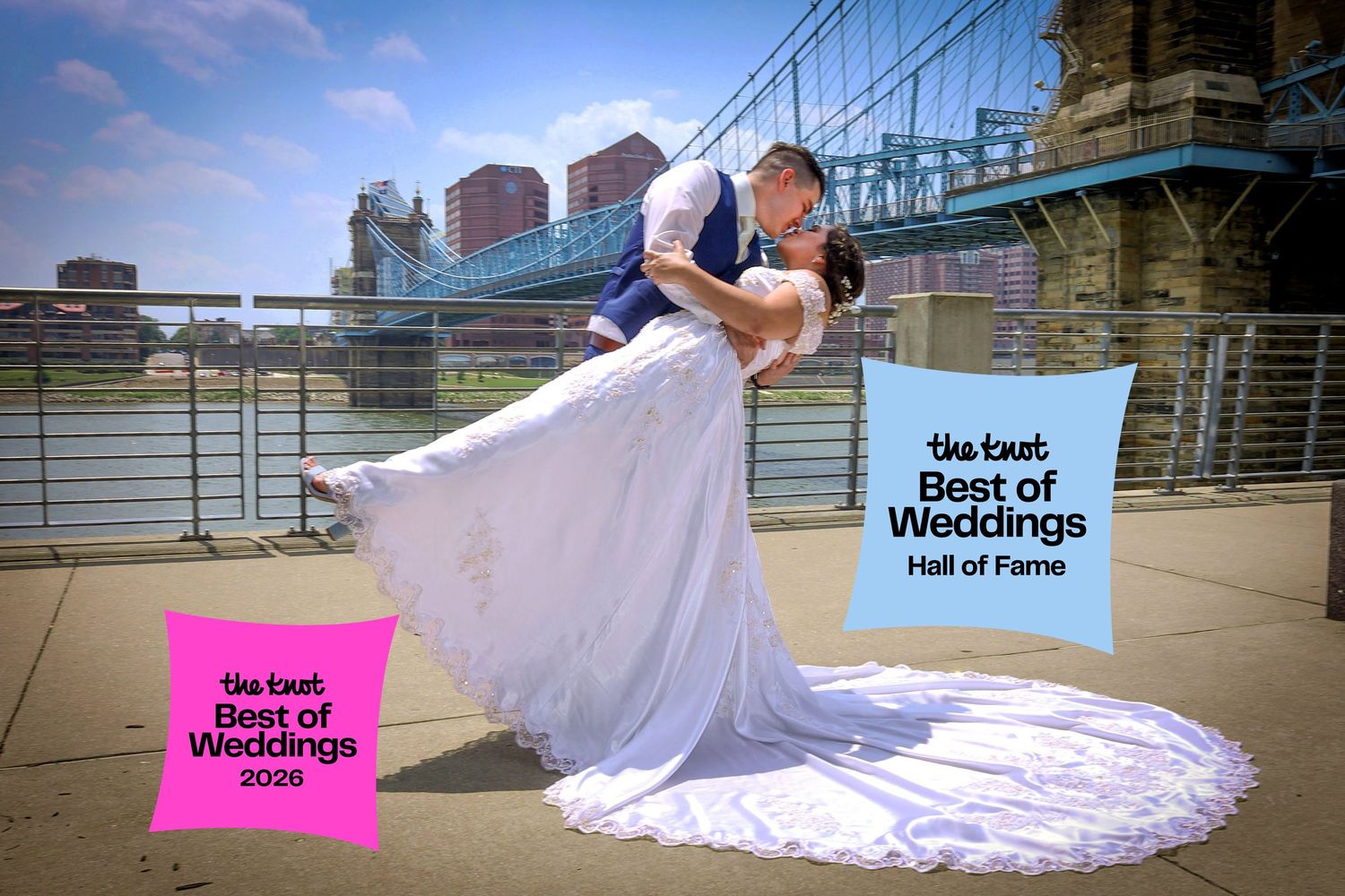 A romantic wedding photo captured on a riverside promenade with city skyline and Best of Weddings signage in view.