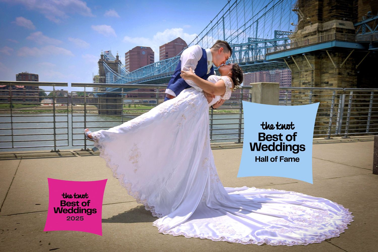 A romantic wedding photo captured on a riverside promenade with city skyline and Best of Weddings signage in view.