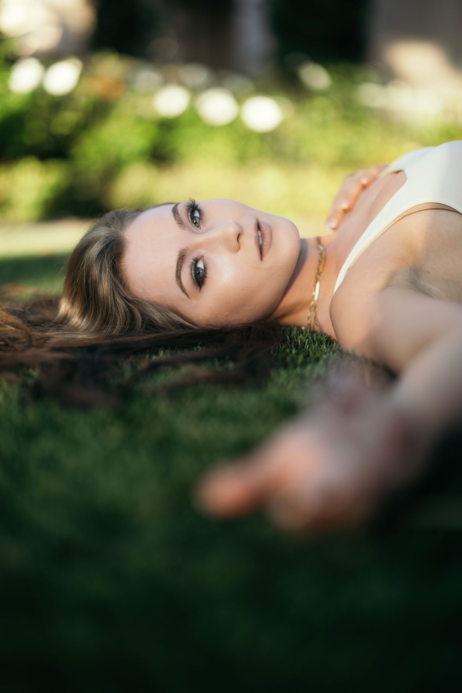 A portrait of someone lying on green grass with soft bokeh lighting in the background.