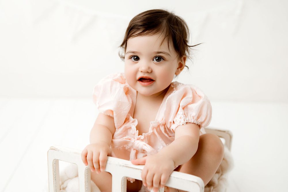 baby girl sitting in a little wooden bed for her first birthday portrait