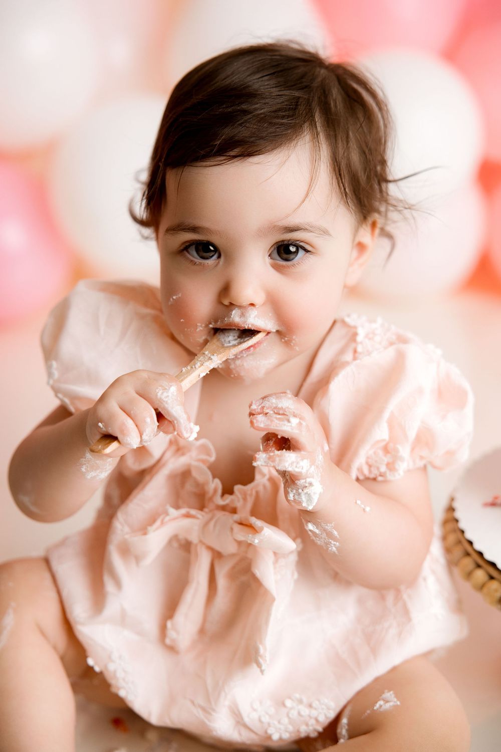 Baby girl first birthday photoshoot, eating a wooden spoon
