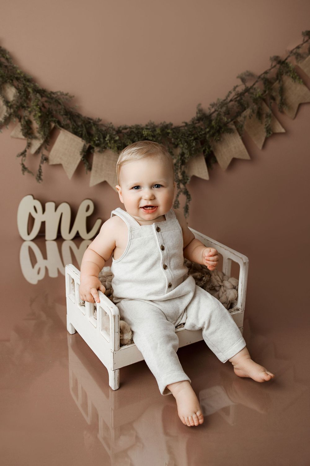 Baby Boy sitting in a little wooden bed, brown background first birthday photos