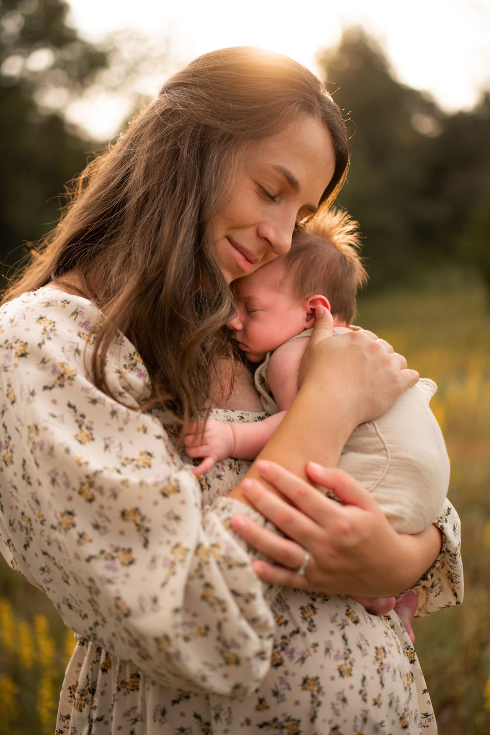 A tender embrace between parent and child at sunset in a wildflower field, wearing floral print clothing during a newborn photo session.
