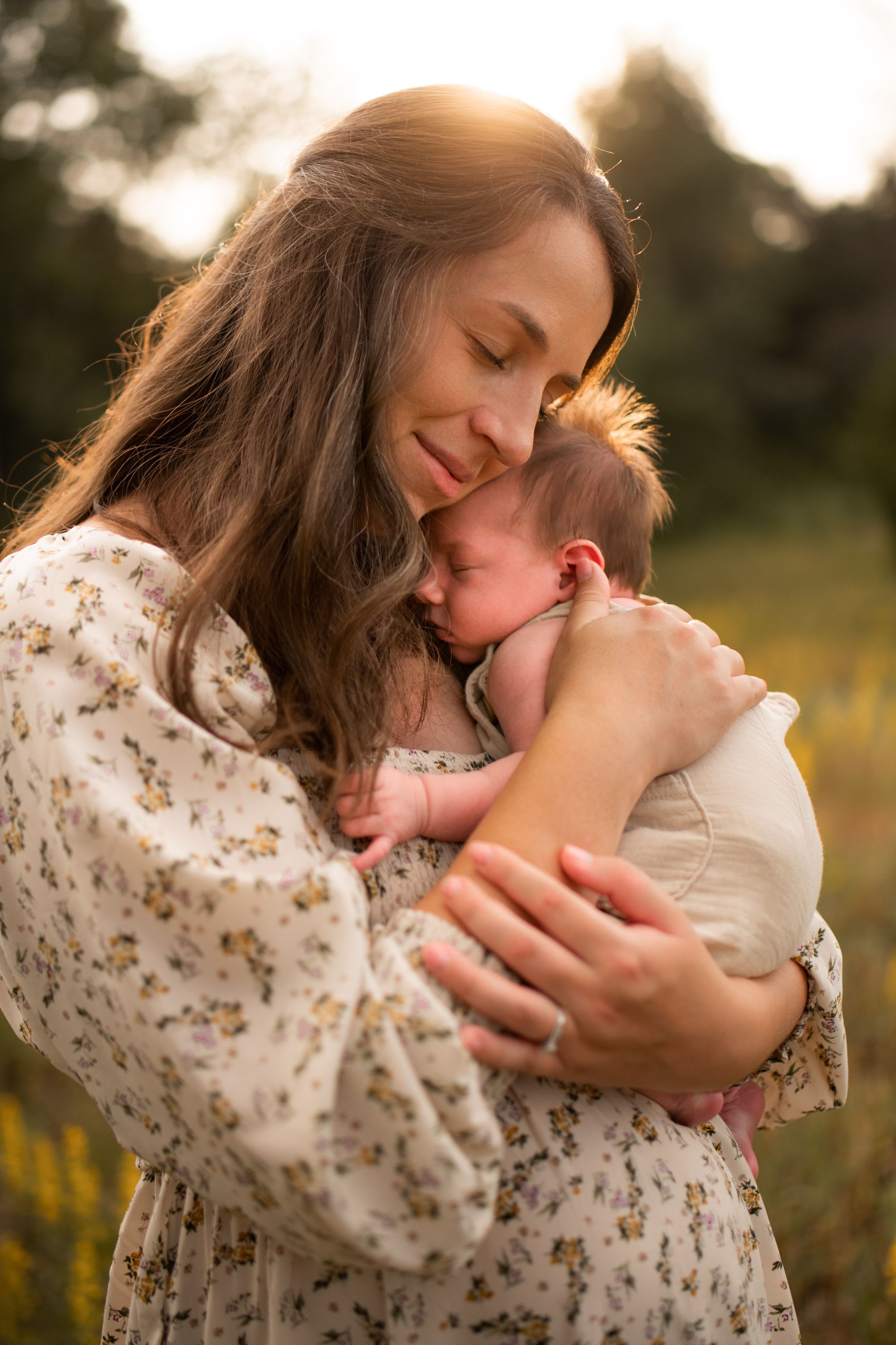 A tender embrace between parent and child at sunset in a wildflower field, wearing floral print clothing during a newborn photo session.