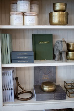 A brand photo session image includes a set of white shelves displaying green books, metallic bowls, and decorative objects in a small shop.