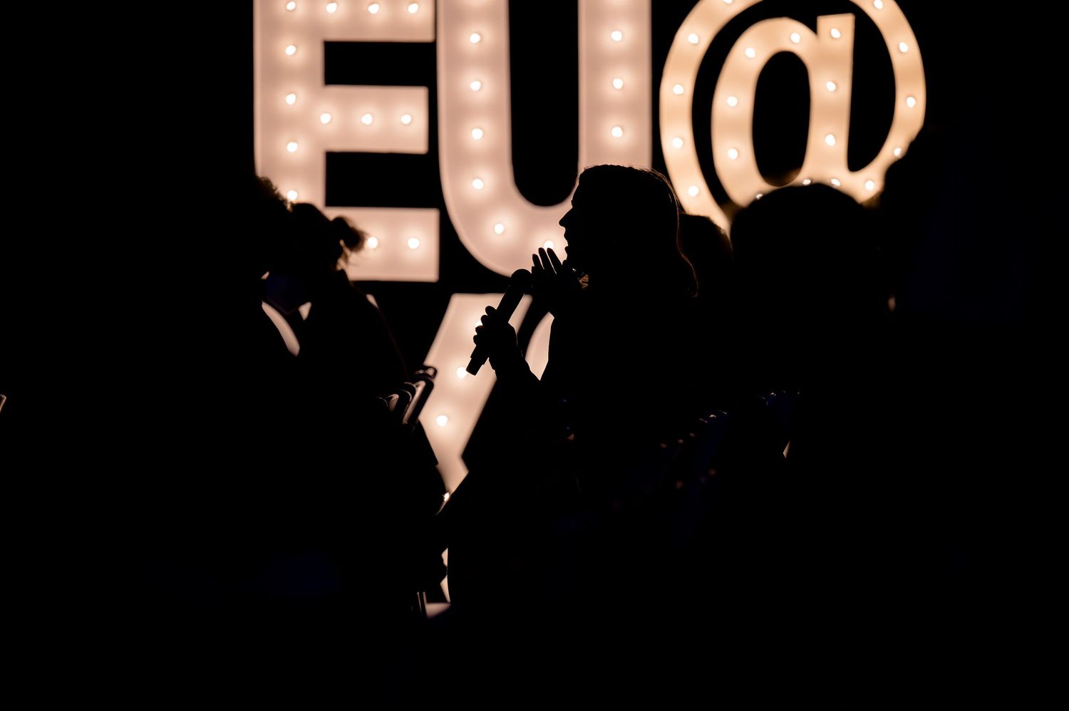 Silhouetted figures dance and celebrate under glowing pink bokeh lights at a festive party or event.