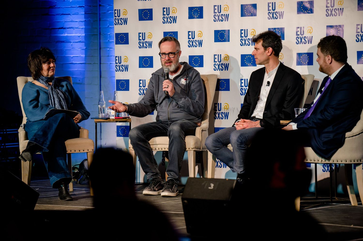 Panel discussion on stage with speakers seated in chairs against blue-lit backdrop at industry conference event.