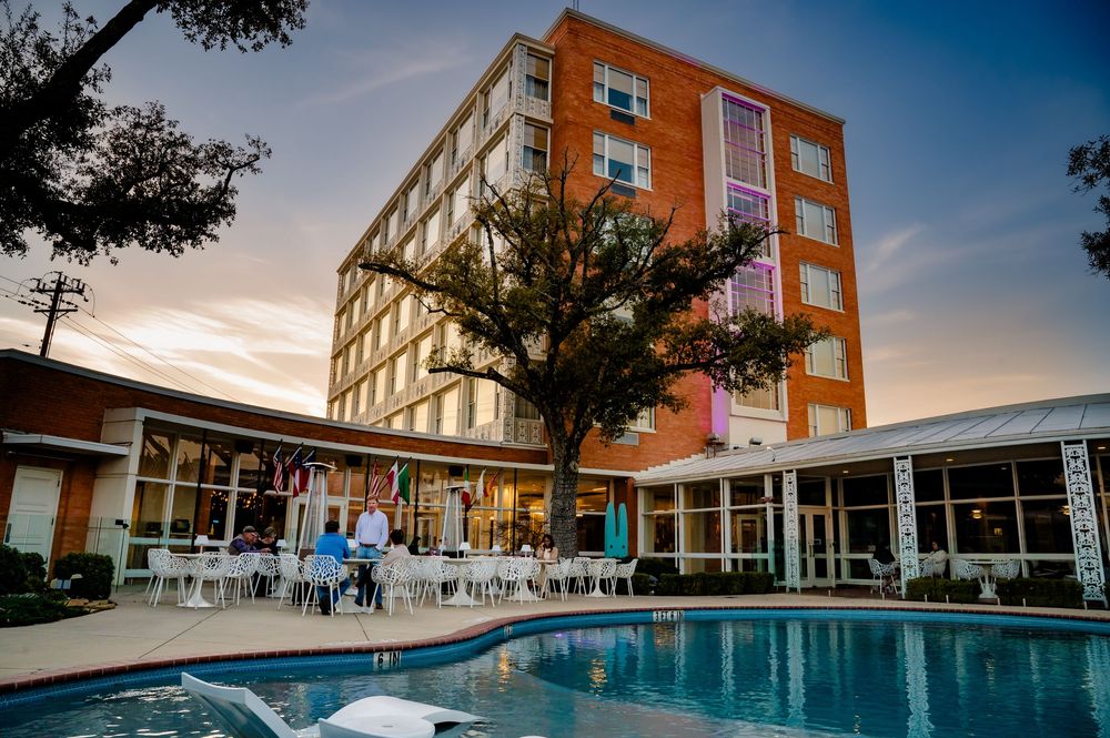 Modern orange apartment building with a pool and courtyard area at sunset against a blue sky.