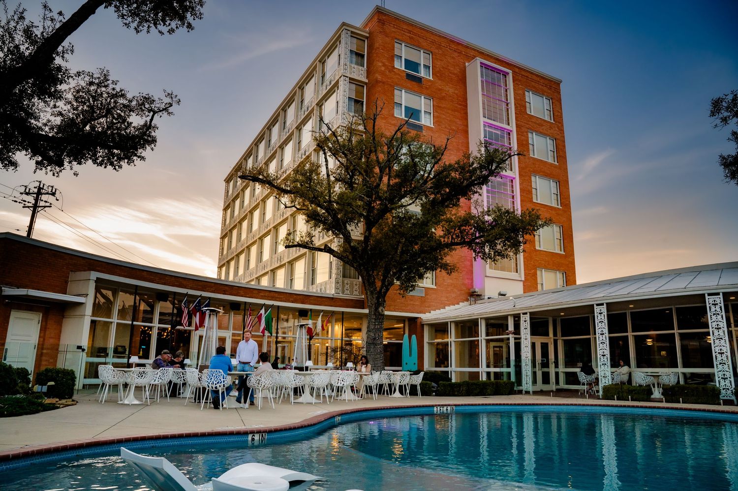 Modern orange apartment building with a pool and courtyard area at sunset against a blue sky.