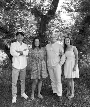 Black and white family portrait of four people standing together under large tree.