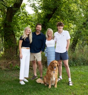 A golden retriever sits with a group in casual summer attire for an outdoor family portrait on a green lawn.