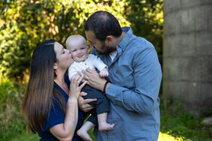 A tender family moment outdoors with a baby being kissed by parents in casual attire.