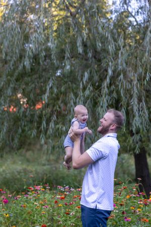 A playful moment between parent and baby against a backdrop of willow trees and wildflowers.