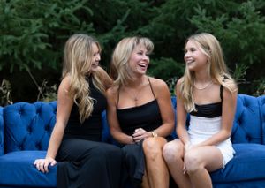 Three people share a candid laugh while sitting on a bright blue velvet couch.