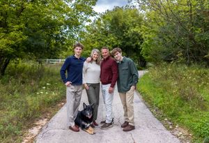 A group stands together with their black dog on a nature path surrounded by green trees and vegetation.