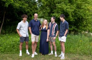 A group poses together outdoors on a summer day with lush green foliage in the background.