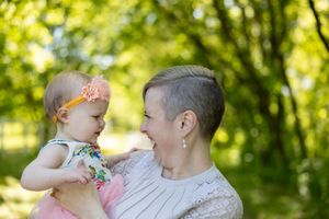 A tender moment shared between adult and baby outdoors with sunlit green foliage in the background.