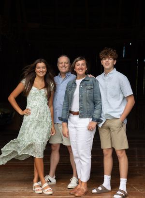A family group poses together on a wooden deck at night wearing coordinated casual summer outfits in white and khaki.