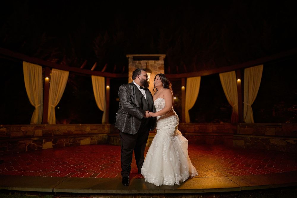 Bride and groom share a romantic moment at night, standing in an elegantly lit outdoor wedding venue.