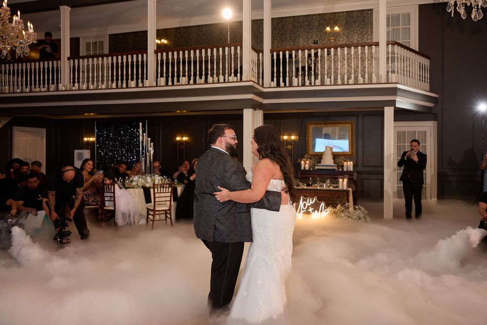 Bride and groom share first dance surrounded by fog machine clouds in elegant ballroom venue.