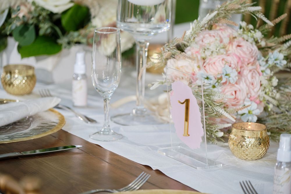 Wedding table decor featuring soft pink flowers, gold accents, and crystal glassware in natural lighting.