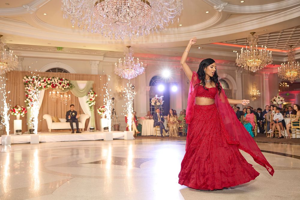 Elegant ballroom decorated with crystal chandeliers and floral arches features a person in a flowing red gown on the dance floor.