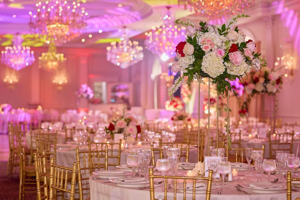 Elegant wedding reception ballroom with pink uplighting, crystal chandeliers, and white floral centerpieces on round tables.
