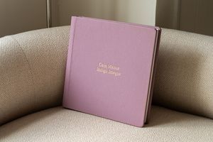 Pink wedding album or photo books arranged on a beige couch or sofa surface with natural lighting.