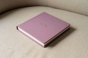 A pink leather-bound book with gold lettering sits on a cream-colored couch cushion.