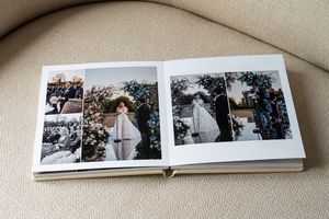 White wedding photo album laid open on light beige sofa showing professional wedding photographs inside.