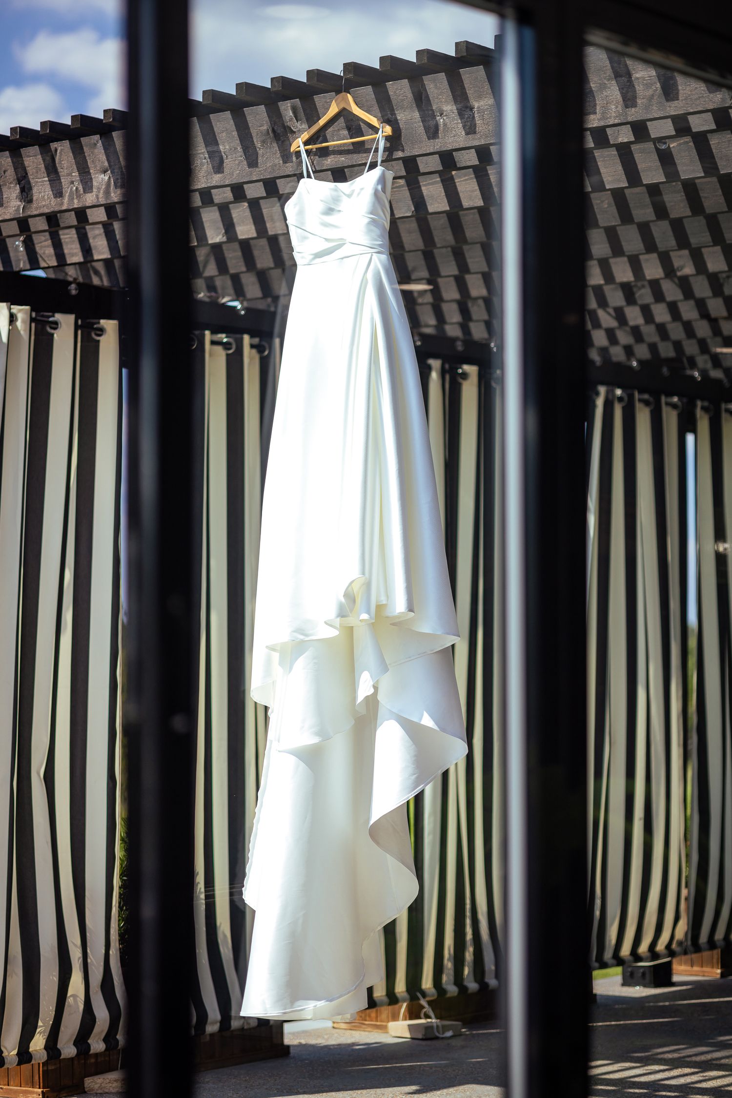 A white wedding dress hangs elegantly on a balcony railing, casting dramatic shadows through the vertical bars.