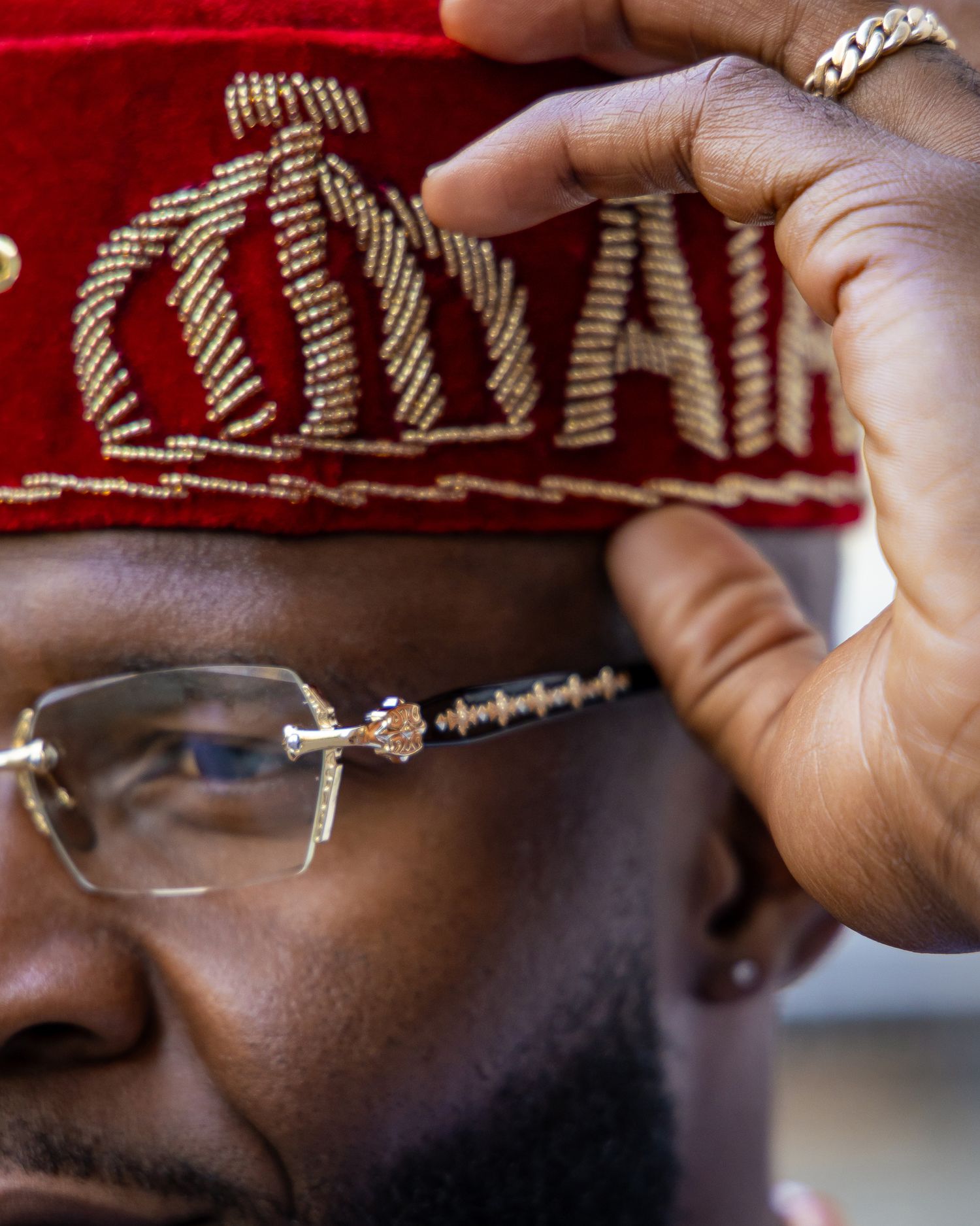 Close-up of hands working on intricate beadwork embroidery on red fabric with metallic thread details.