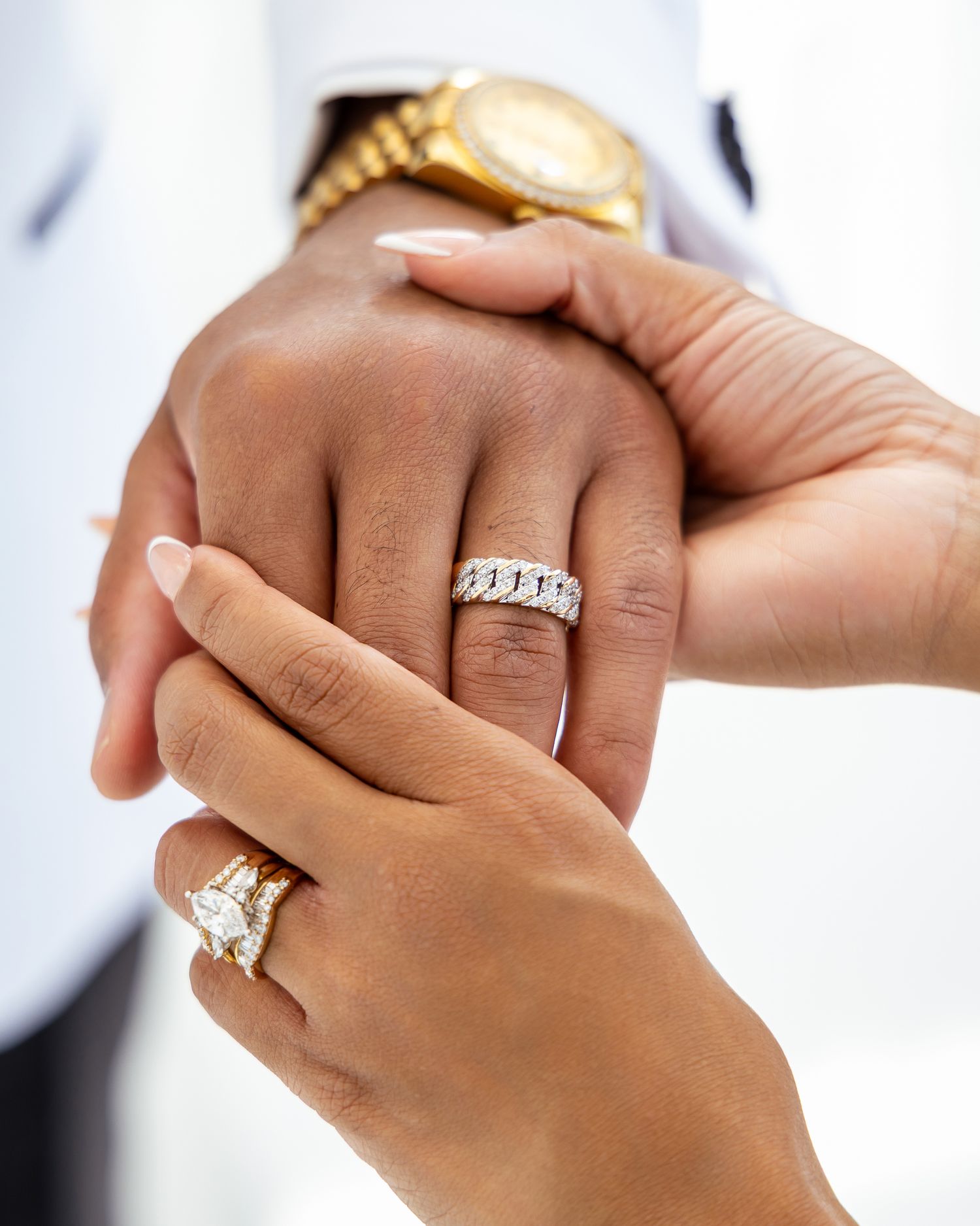 Close-up view of hands wearing engagement rings with diamond solitaires against a light background.