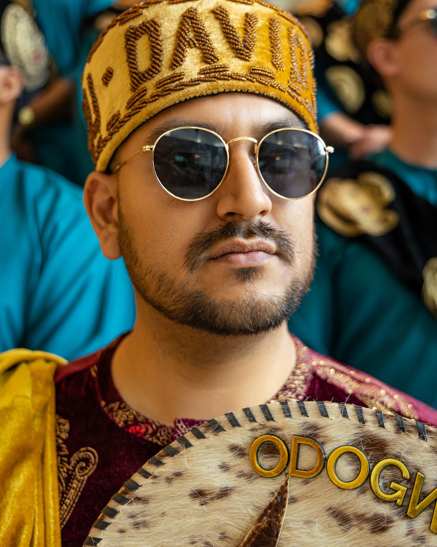 Person wearing a yellow headband with text, round sunglasses, and burgundy patterned clothing in an outdoor setting.