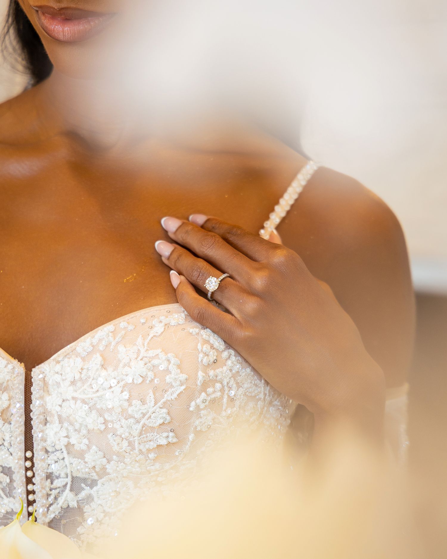 A close-up view of a delicate white lace wedding dress bodice with intricate floral patterns and beading details.