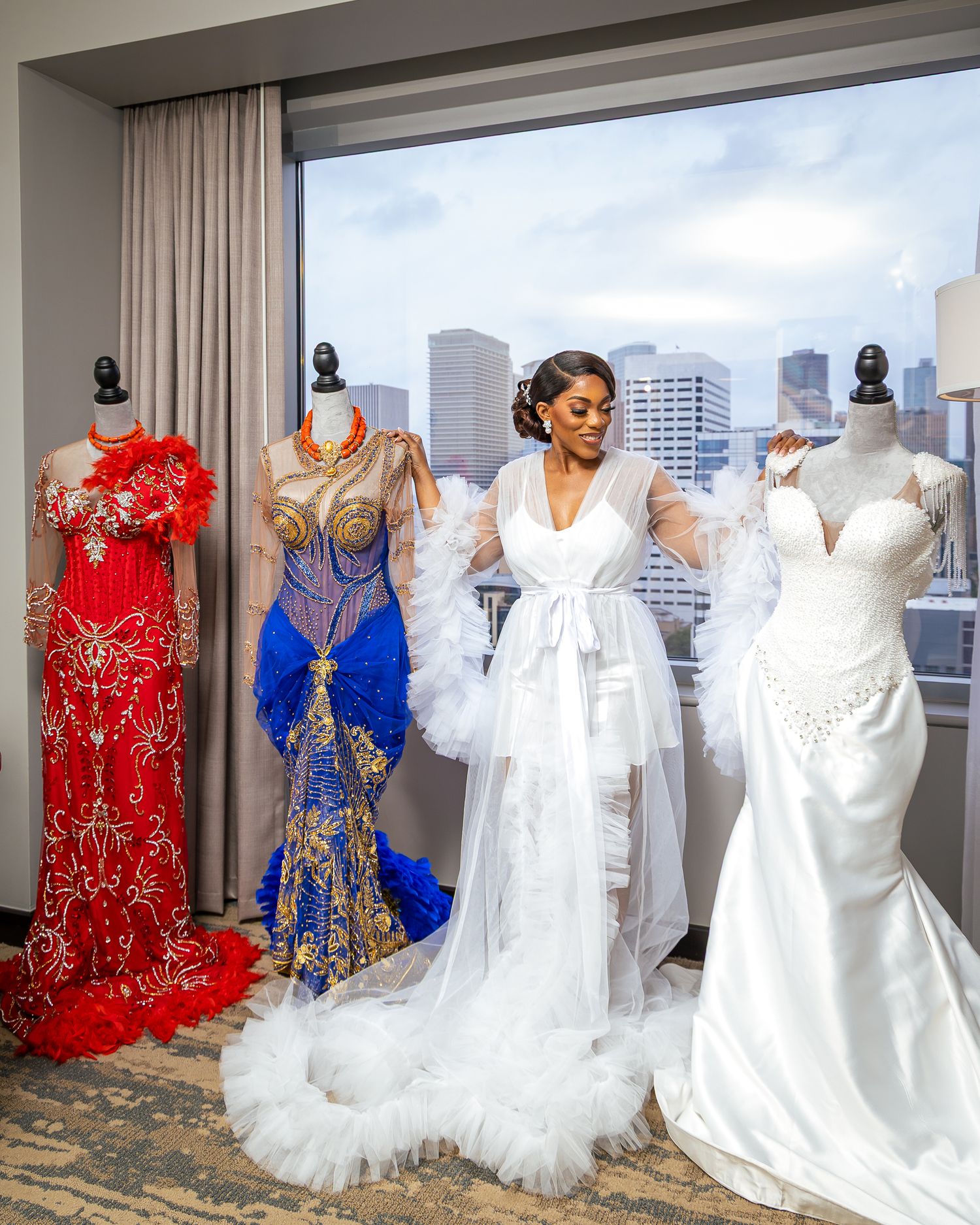 A row of elegant wedding dresses and formal gowns on display in a bridal boutique with city views through the windows.