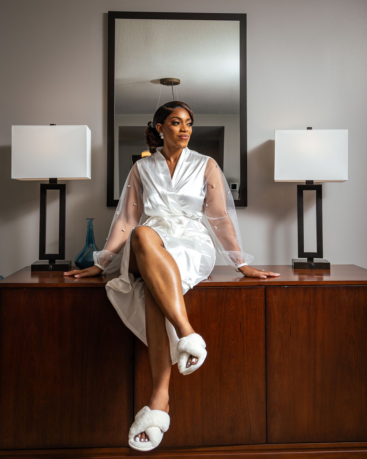 A person in a white robe lounges on a wooden credenza with table lamps, shown in a series of artistic poses.