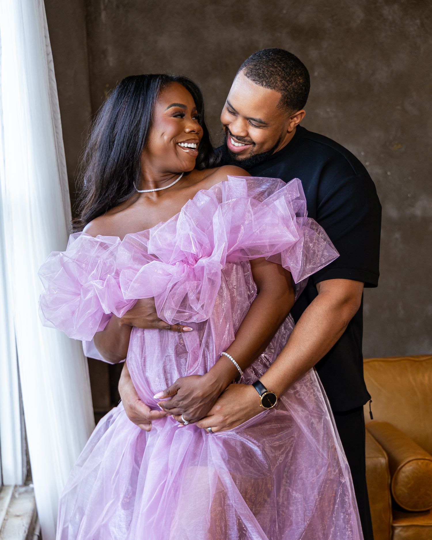 A couple shares a tender moment in an engagement photoshoot, with the woman wearing a flowing pink tulle dress.