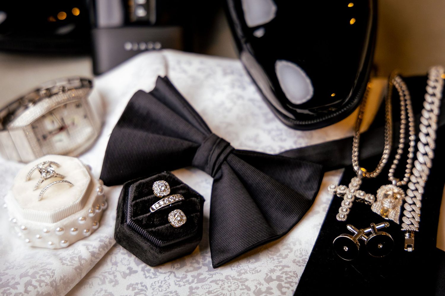 Black satin bow ties and silver jewelry accessories arranged on a reflective surface in elegant wedding styling.