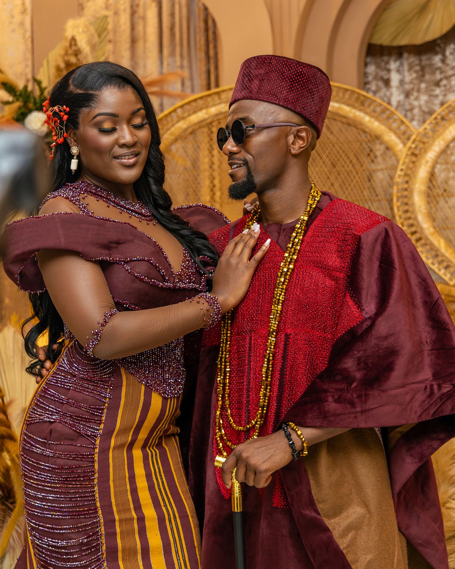 Couple in traditional African wedding attire embracing in an ornate gold-decorated venue during their celebration.