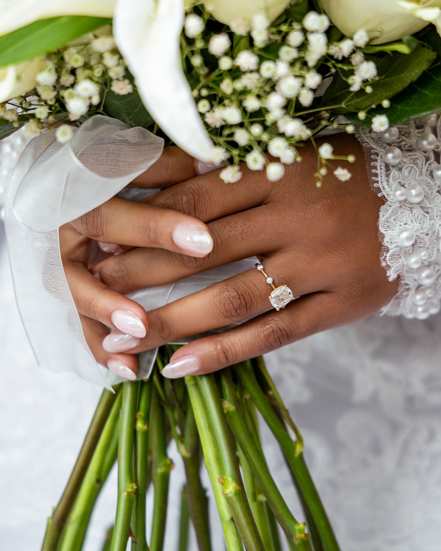 Close-up of hands holding a white and green wedding bouquet with baby's breath flowers and rings on display.