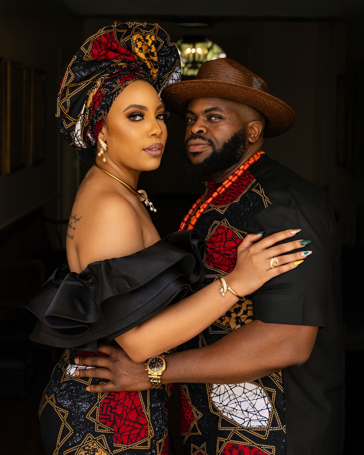A couple in traditional African-inspired attire with red and black ankara print fabric pose together in a romantic portrait.