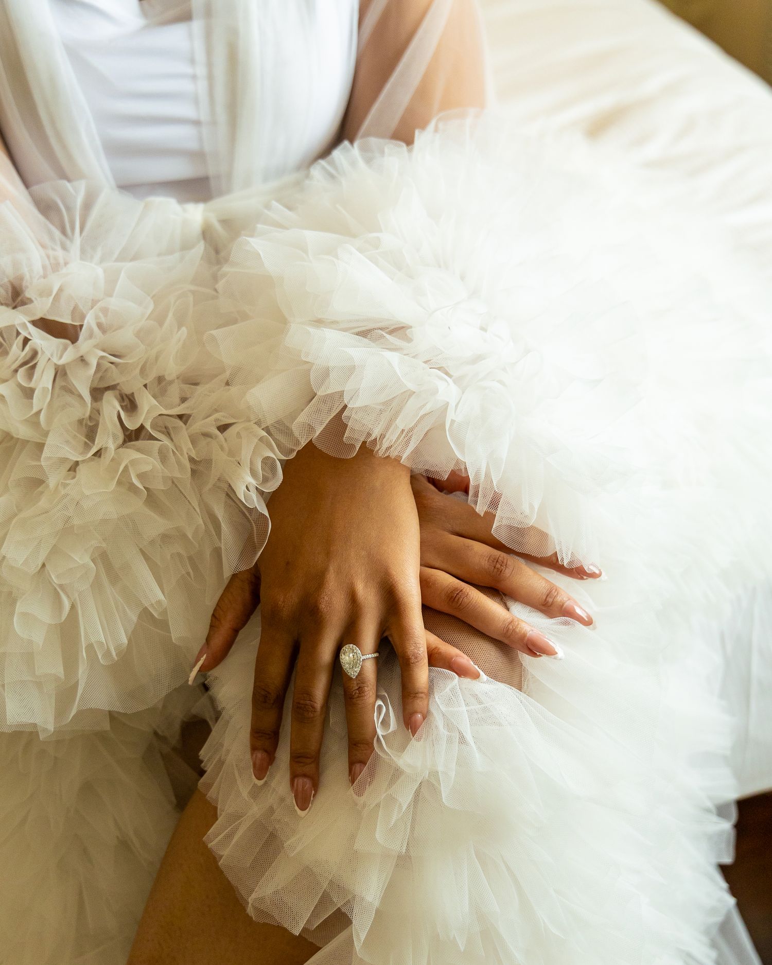 Close-up detail shots of hands resting on layers of white tulle fabric from a wedding dress.